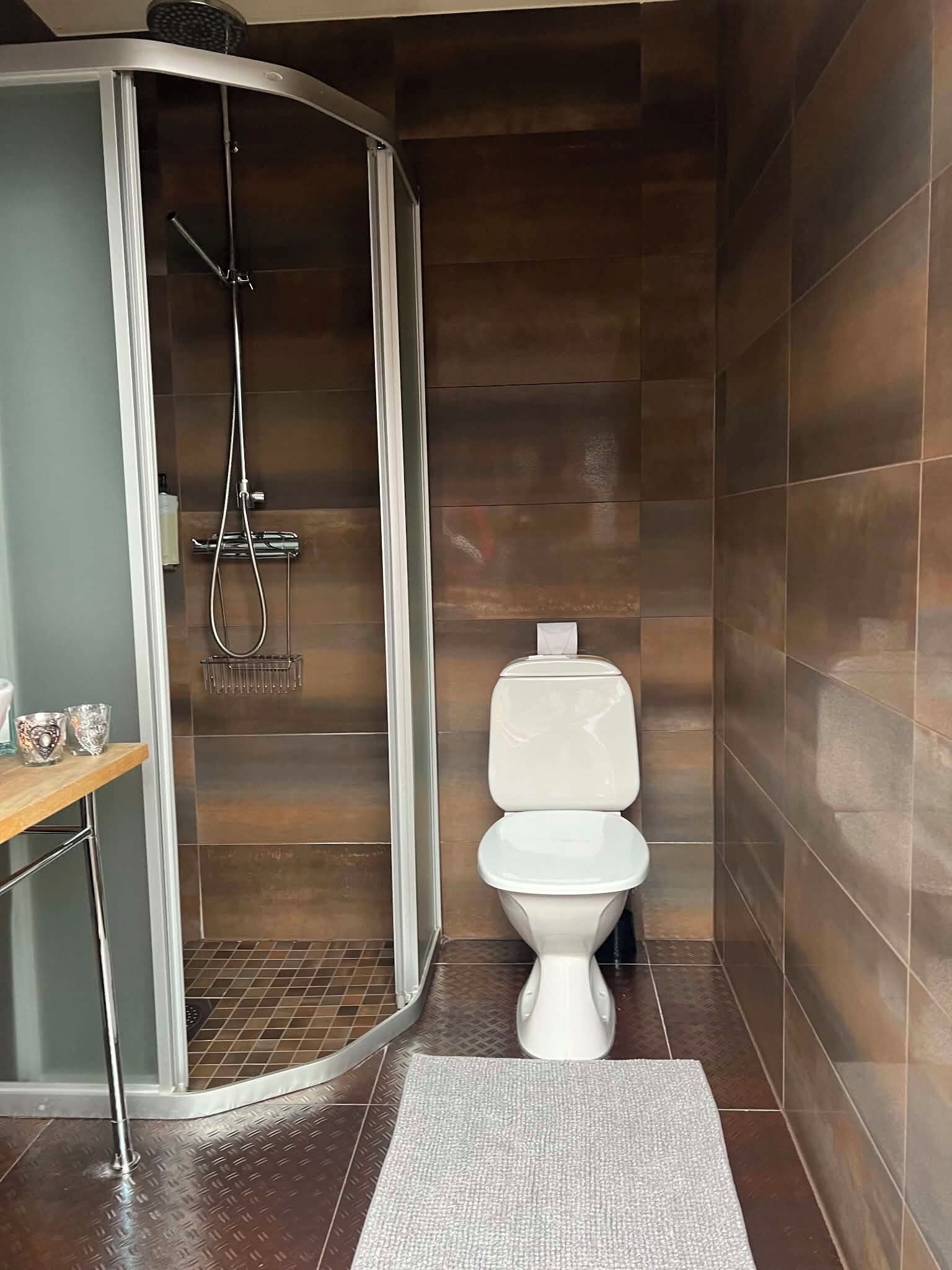 Een badkamer met een douche, toilet en een klein plankje met glazen.