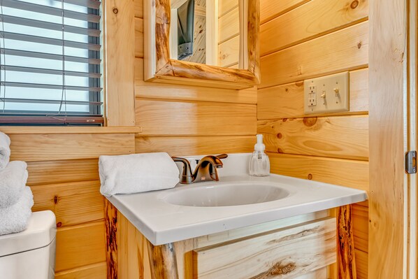 A wooden cabin bathroom with a white sink, a mirror, and a window with blinds.