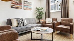 A modern living room with a grey sofa, a round coffee table, and two leather armchairs. There are abstract paintings on the wall and a potted plant in the corner. - Host & Stay | Slater Street Apartment IV (Liverpool)