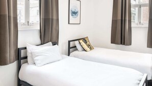 Two single beds with white linens and dark frames in a room with large windows and brown curtains. - Host & Stay | Slater Street Apartment IV (Liverpool)