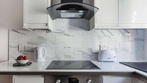Uma cozinha moderna com armários brancos, forno embutido, fogão e máquina de café.