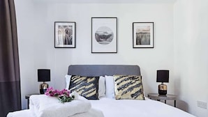 Quarto de hotel bem arrumado com uma cama grande, duas mesas de cabeceira com luminárias e três quadros na parede.