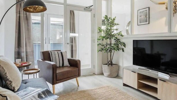 Ein modernes Wohnzimmer mit einer braunen Ledersofa, einem großen Flachbildfernseher, einer Topfpflanze und einem minimalistischen Design.