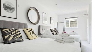 Ein Hotelzimmer mit einem großen Bett, einem grauen Kopfteil, einem runden Spiegel und einem Fenster mit Jalousien.