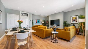 A modern living room with a dining area, featuring a sofa set, a dining table with chairs, and a TV mounted on the wall. - Host & Stay | Upper Duke Street Apartment (Liverpool)