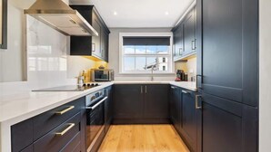 A modern kitchen with dark cabinetry, a white countertop, and a window providing natural light. - Host & Stay | Upper Duke Street Apartment (Liverpool)