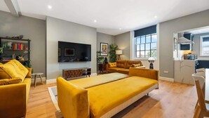 A modern living room with a sofa set, a flat-screen TV mounted on the wall, a small side table, and a window with a view. - Host & Stay | Upper Duke Street Apartment (Liverpool)