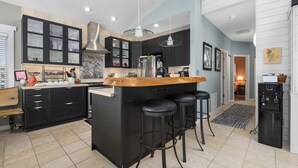 Una cocina moderna con gabinetes negros, una isla central con taburetes, horno empotrado y dispensador de agua.