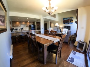 Een ruime eethoek met een houten tafel en stoelen, een kroonluchter en een keuken op de achtergrond.