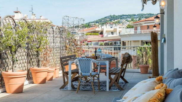 A rooftop terrace with a table and chairs, potted plants, and a view of the cityscape.