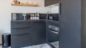 A modern kitchen with dark cabinetry, a built-in oven, and a coffee maker.