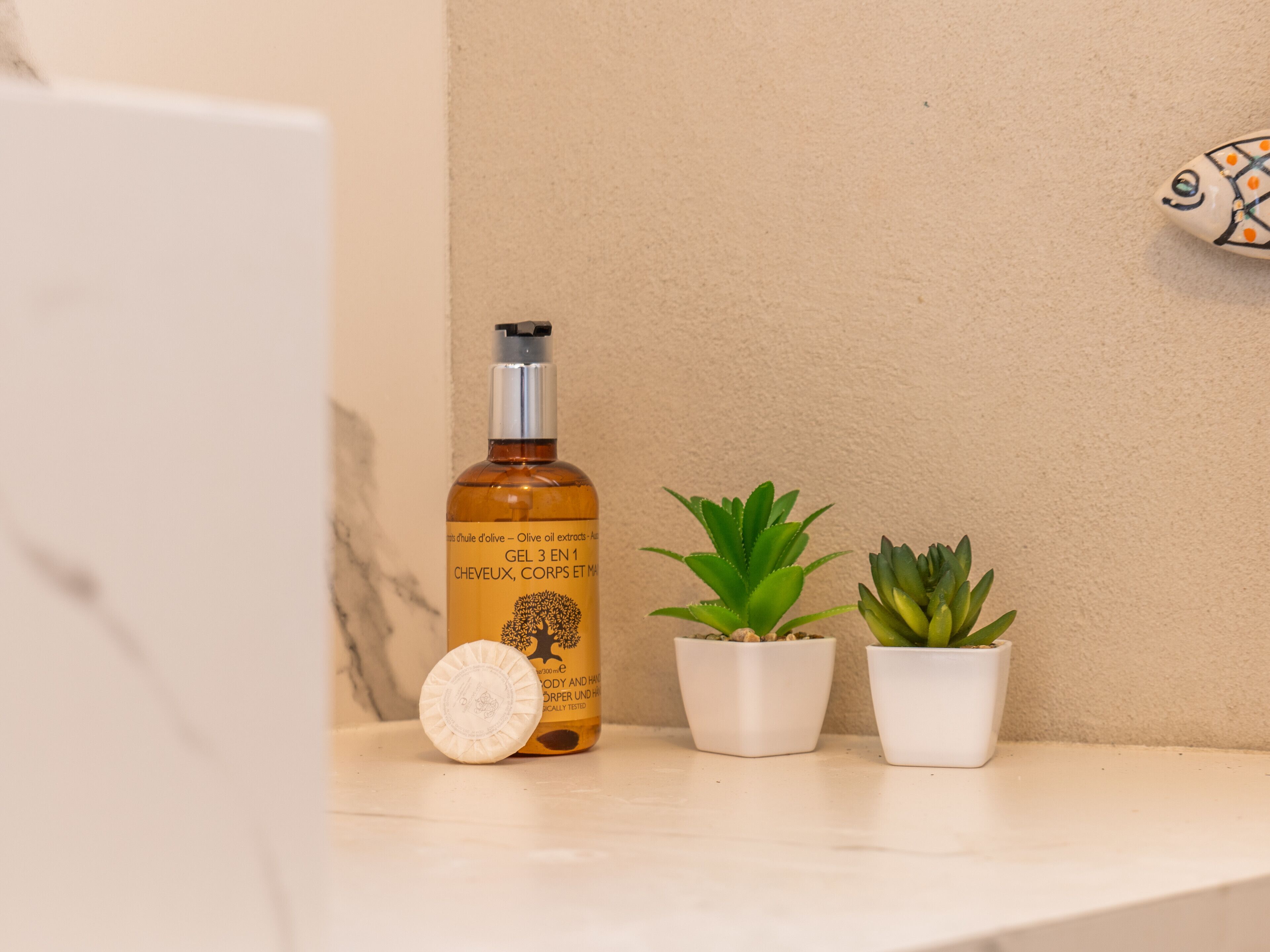 A bathroom shelf with a bottle of olive oil extract, two potted plants, and a soap bar.