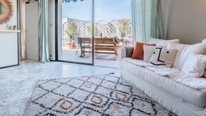 A modern living room with a sofa, a patterned rug, and a sliding glass door leading to an outdoor patio with a table and chairs.