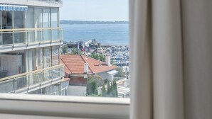 A view from a window overlooking a marina with boats, a clear sky, and buildings with red-tiled roofs.