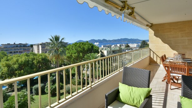 Un balcon doté de meubles en osier et offrant une vue sur la mer et les bâtiments.