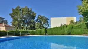 Une piscine à l’eau d’un bleu cristallin, entourée de verdure, avec un bâtiment visible au loin.