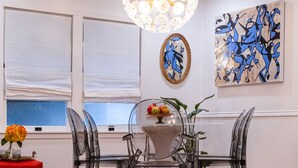 Un coin repas comprenant une table ronde, des chaises, un lustre, des œuvres d’art et une fenêtre avec des stores.