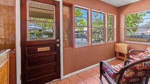 A room with a wooden door marked 'EXIT', large windows, a small table, and wicker chairs. - Lincolnville Cottage | Sunroom & Fenced Yard (St. Augustine)