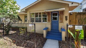 A single-story house with a beige exterior, a blue front door, and a small porch with a white railing. - Lincolnville Cottage | Sunroom & Fenced Yard (St. Augustine)