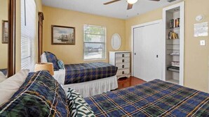 A bedroom with two beds, a ceiling fan, a window with blinds, a dresser, and a bookshelf. - Lincolnville Cottage | Sunroom & Fenced Yard (St. Augustine)