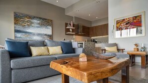 Een moderne woonkamer met een grijze bank, een houten salontafel en kunstwerken aan de muur.