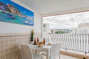 A balcony with a table set for two, a potted plant, and a painting of a coastal scene. - Polly House by Wonderful Italy (Polignano a Mare)