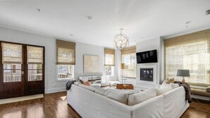 A spacious living room with a large white sectional sofa, a fireplace, and a television mounted on the wall.