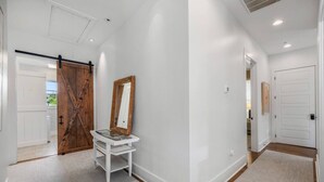 A hallway with a white door, a wooden door, a white bench, and a mirror.