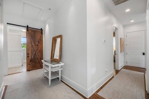 A hallway with a white door, a wooden door, a white bench, and a mirror. - Les Bons Temps on Minnich
(Heart of Downtown) (Fairhope)