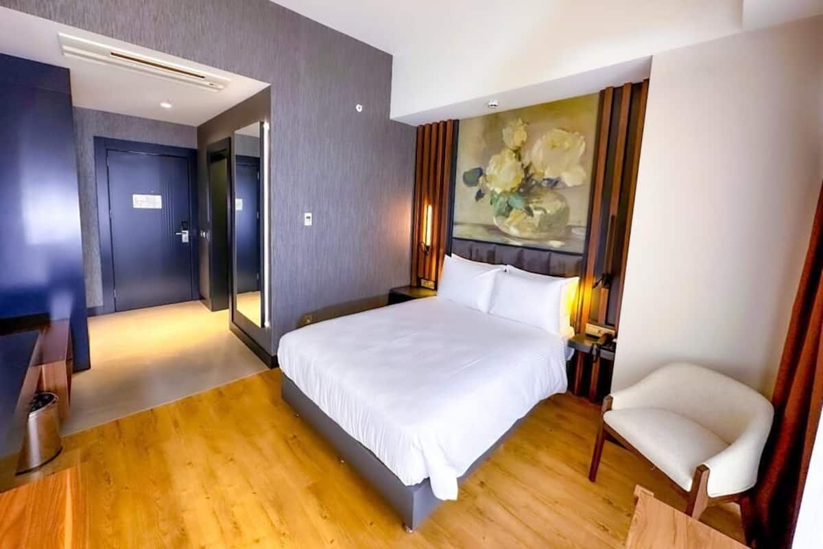 A modern hotel room with a large bed, a desk, a chair, and a painting on the wall.