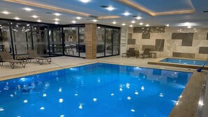 An indoor swimming pool with clear blue water, surrounded by lounge chairs and a glass-enclosed area with seating. - S Class Hotel Convention Center (Gaziantep)