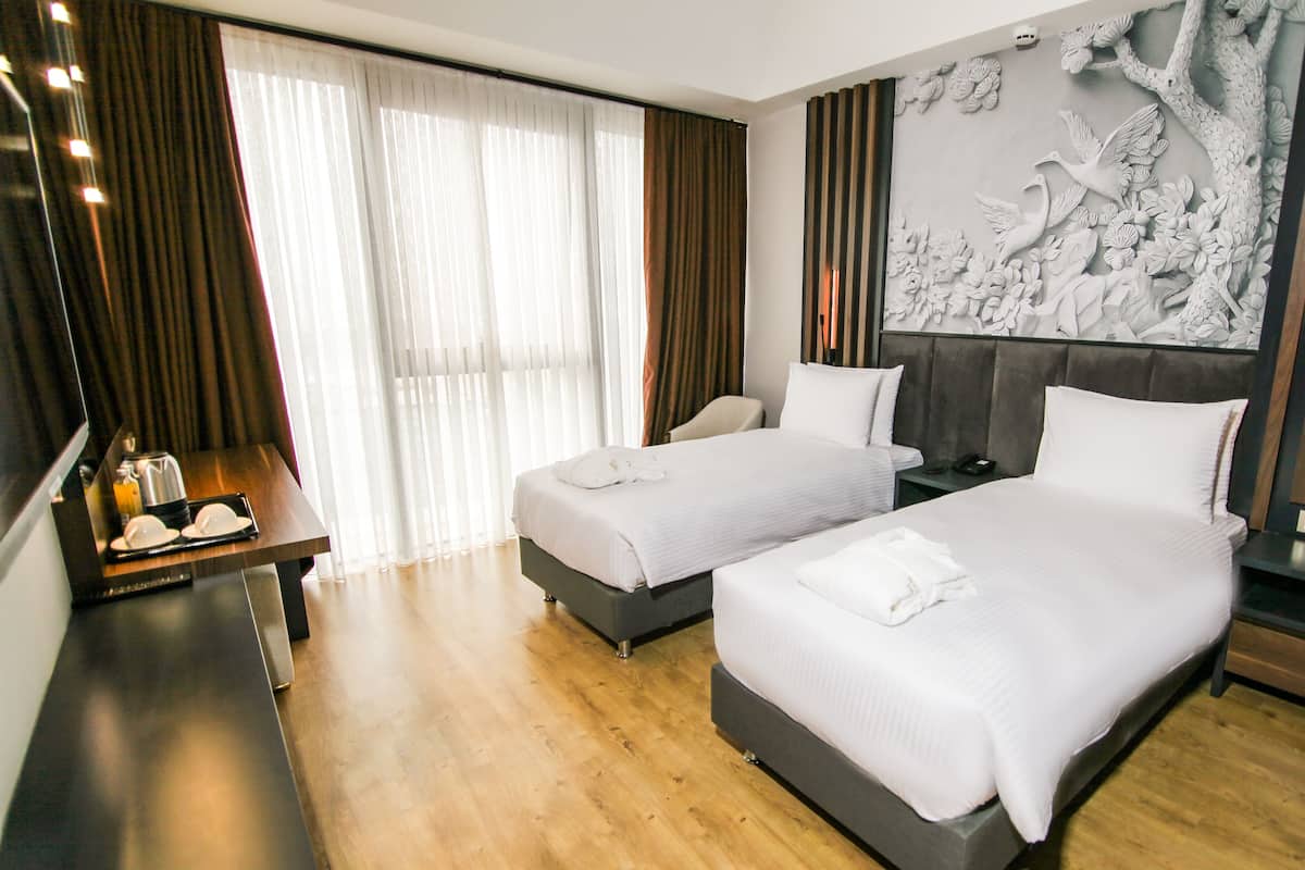 A hotel room with two beds, a desk with a lamp, a mirror, and a decorative wall panel.