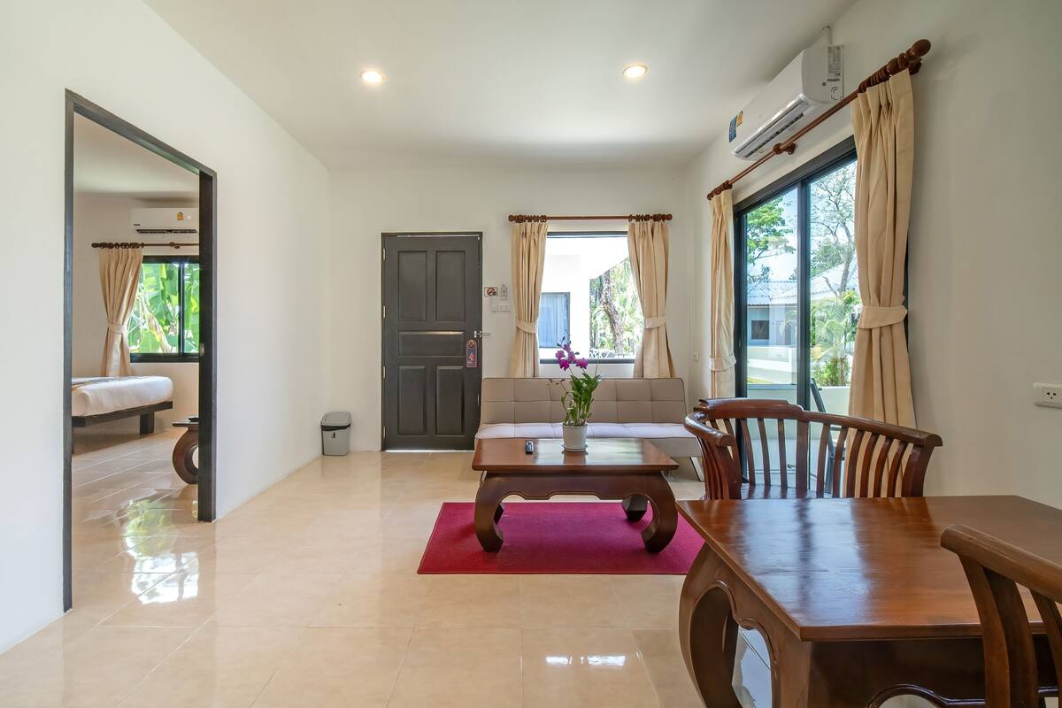 A spacious living area with a wooden dining table, a sofa, and a large window with curtains.