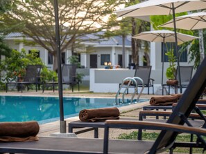 A poolside area with lounge chairs and umbrellas, a pool, and a building in the background. - Isara Nai Yang Resort (Sa Khu)