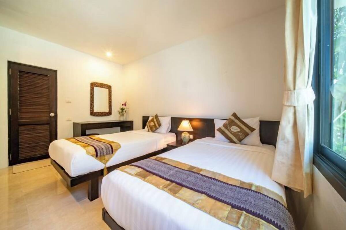 A hotel room with two beds, a nightstand, a mirror, and a window with curtains.