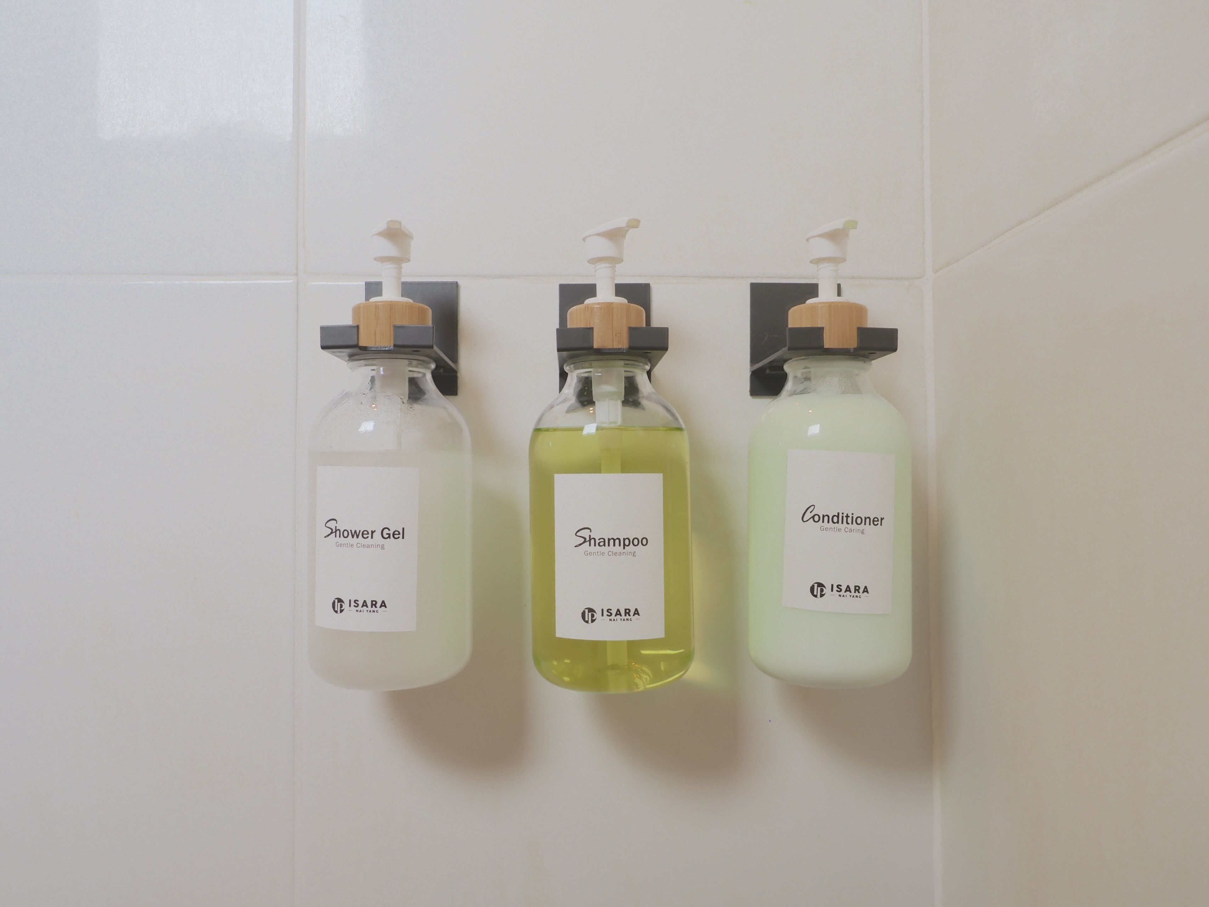 Drei Flaschen Duschgel, Shampoo und Spülung hängen an einer Wand.