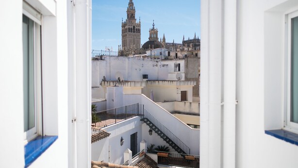 Vista de un edificio histórico con una torre destacada, a través de una ventana con paredes blancas y detalles azules.