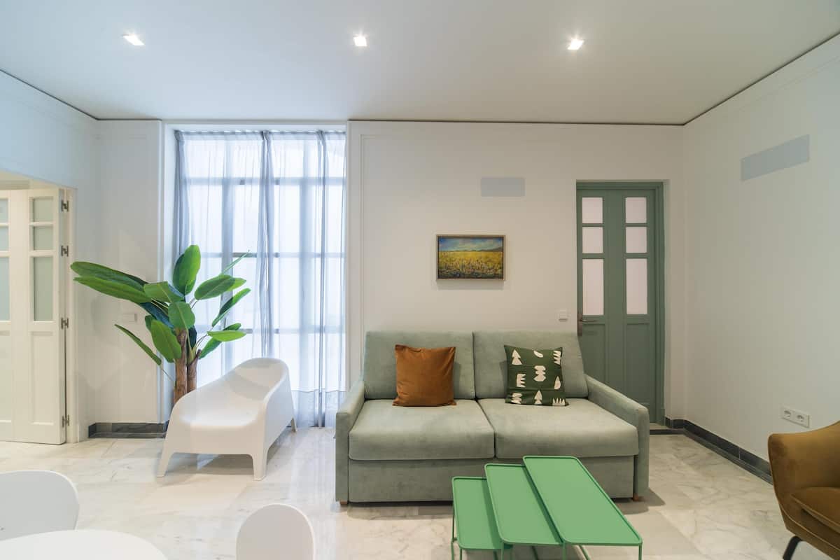 A modern living room with a sofa, a dining table, and a large window with curtains.