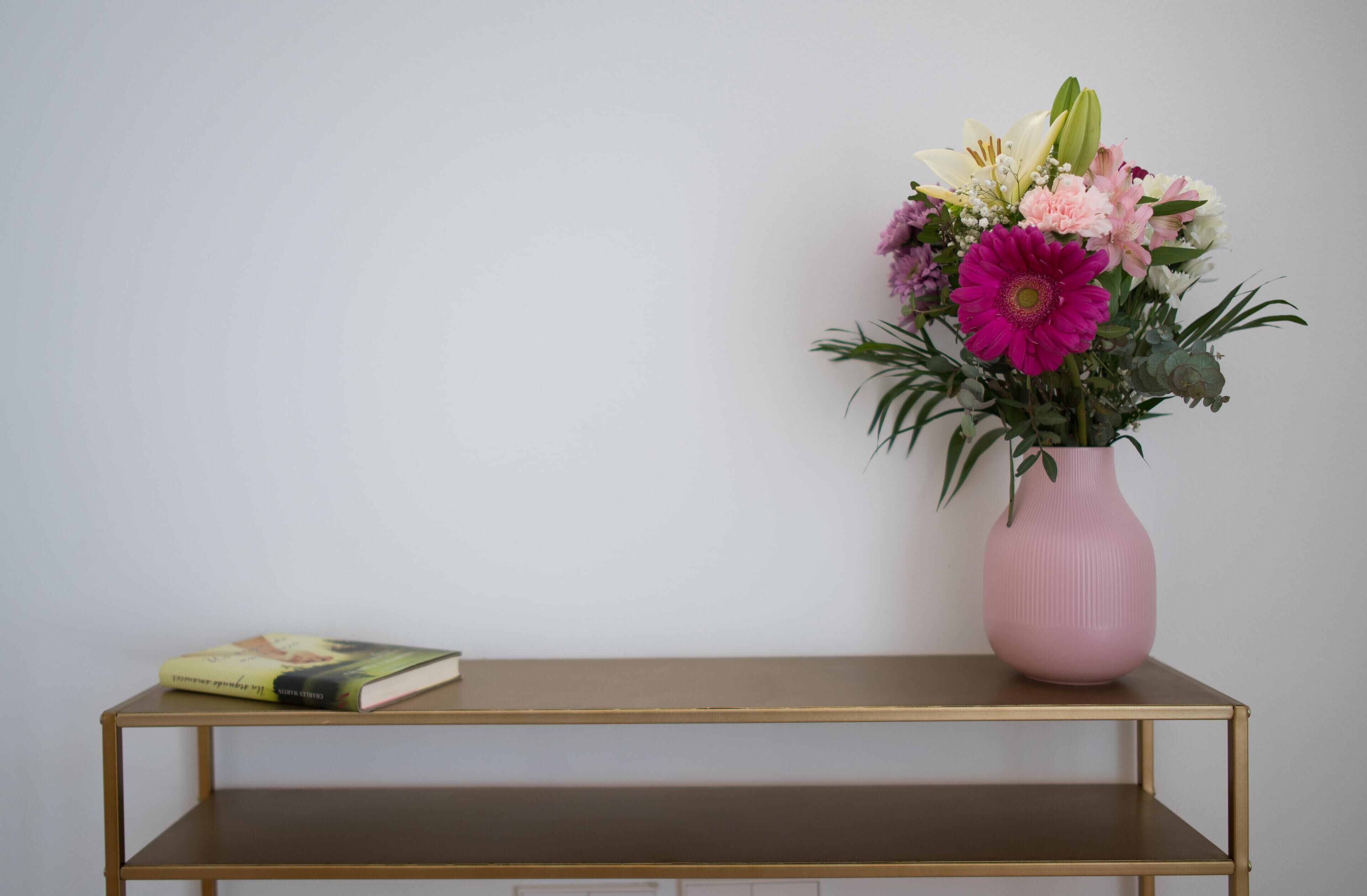 Un vase rose orné de fleurs, posé sur une étagère.