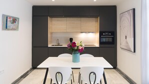 Una cocina moderna con armarios oscuros, horno empotrado y comedor con mesa y sillas blancas.