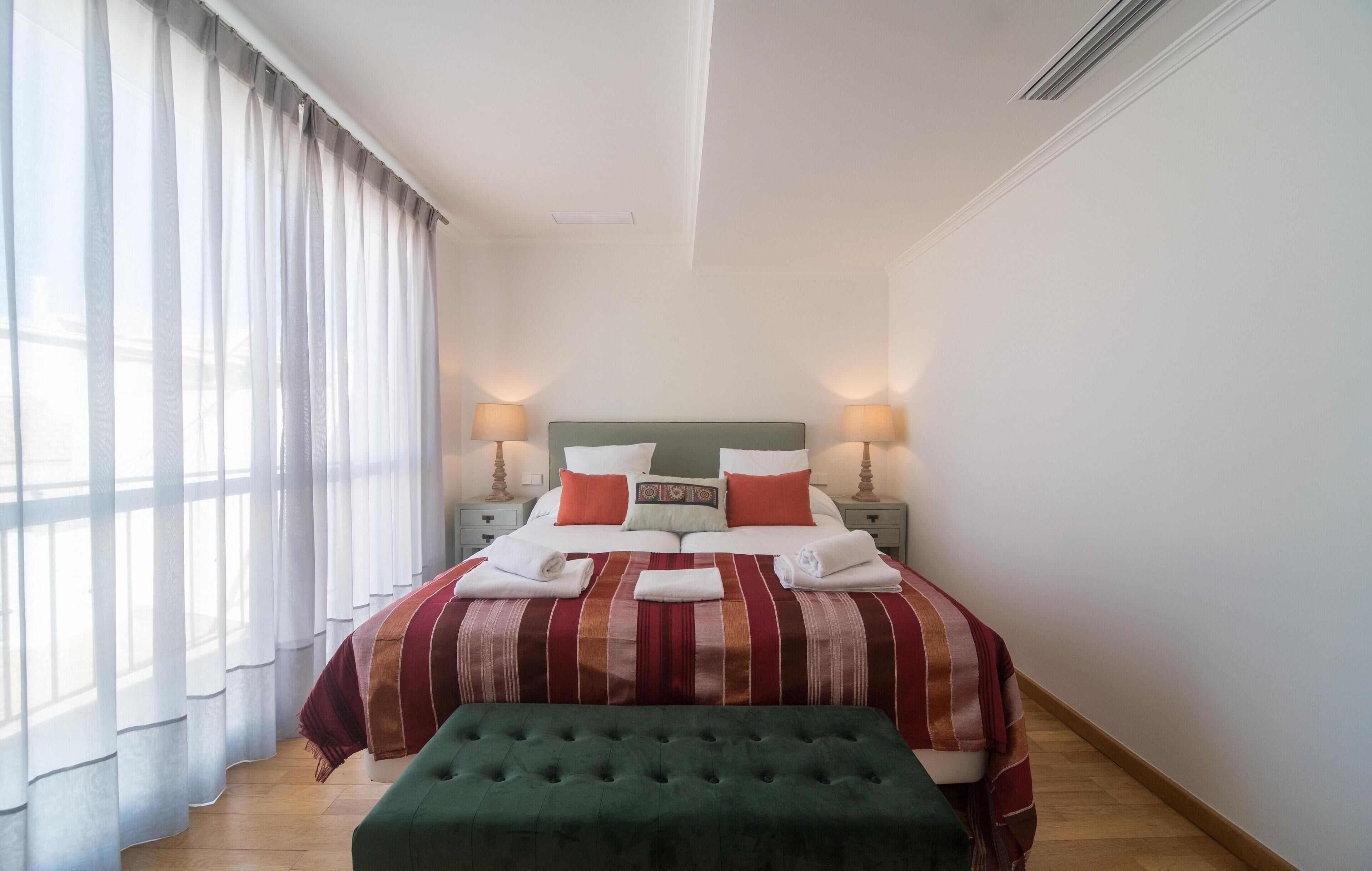 A neatly made bed with a striped bedspread, pillows, and two bedside lamps.