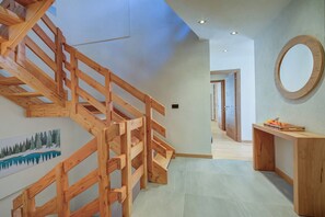 Una escalera de madera que conduce a un segundo piso, un pasillo con un banco de madera y un espejo redondo en la pared.