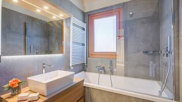 A modern bathroom with a large mirror, a rectangular sink, a bathtub, and a glass-enclosed shower.