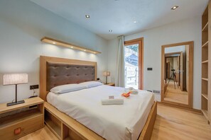 A modern hotel room with a large bed, wooden headboard, bedside tables, and a mirror. - Chalet Merveille Ski In - Ski Out (Sauze d'Oulx)