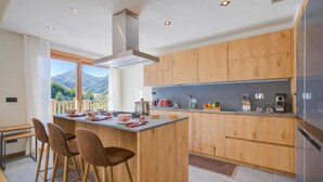 Una cucina moderna con mobili in legno, un'isola centrale con sgabelli da bar, un'ampia finestra vista montagna e un piano cottura integrato.