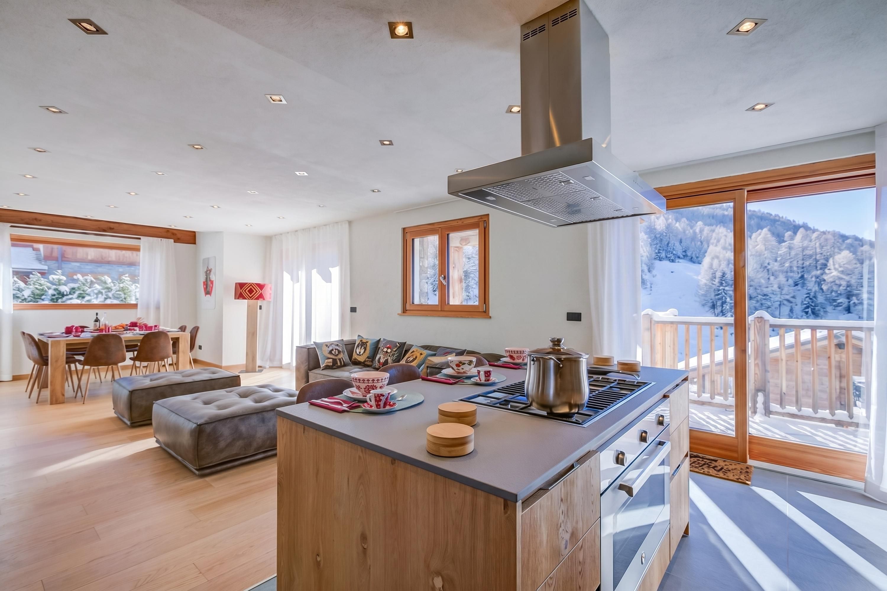 A modern kitchen with a central island, dining area, and a view of a snowy landscape.