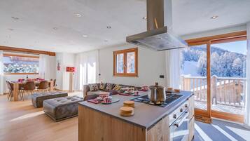 A modern kitchen with a central island, dining area, and a view of a snowy landscape.