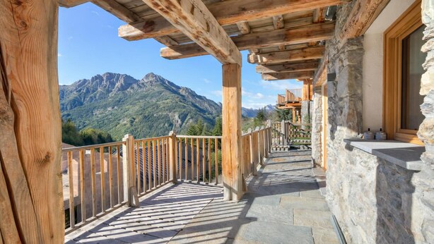 Un balcone in legno con pavimento in pietra, affacciato su un paesaggio montano.