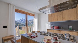 Una cucina moderna con vista sulle montagne, armadietti in legno e un'area pranzo con tavolo apparecchiato per due.