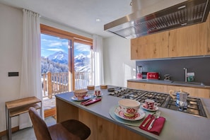 A modern kitchen with a gas stove, wooden cabinets, and a view of mountains through the window. - Chalet Merveille Ski In - Ski Out (Sauze d'Oulx)